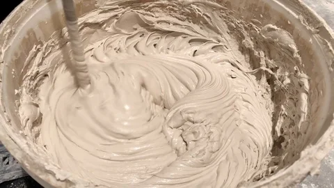 Worker mixing plaster solution in a bucket, using an electric drill. Video stock 122303115