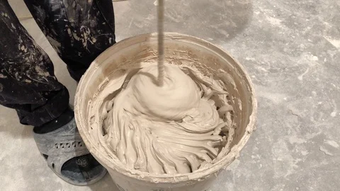 Worker mixing plaster solution in a bucket, using an electric drill. Video stock 122303177