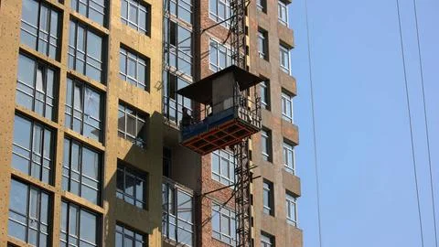 Worker move down on the construction elevator lift. Stock Photos