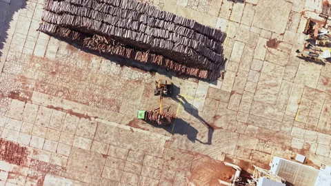 Worker moves materials across a stone paved site beside rows of stacked roof Stock Footage 348052511