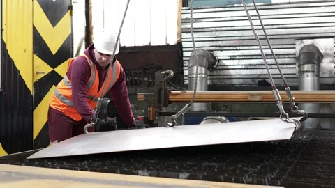 A worker moves metal using an overhead crane to a metal plasma cutting machine. Stock Footage 273045360