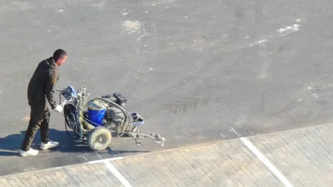 Worker moves paint sprayer in industrial area near shipping container for mainte Stock Footage 337530824