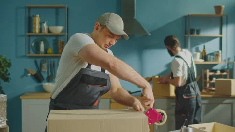 Worker of Moving Company Using Duct Tape Machine for Packing a Cardboard Box. Stock Footage 241386299