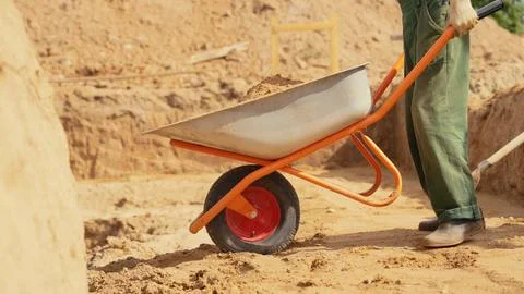 Worker moving soil with wheelbarrow at construction site Stock Photos