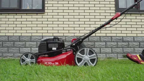A worker mows the lawn pushing a lawn mower along the house Stock Footage 137978478