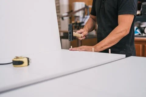 Worker nailing studs with a hammer to a piece of furniture in a workshop Stock Photos