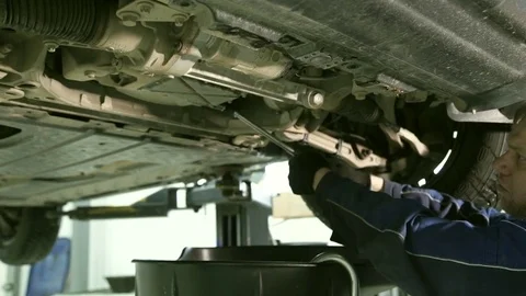 Worker opens lid, oil flows from the bottom of car in garage Stock Footage 76531332