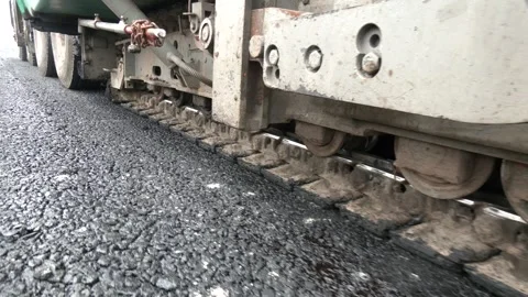 Worker operates an asphalt paving machine as it lays down fresh asphalt Stockbeeldmateriaal 330351046