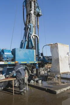A worker operates a drilling rig close-up at a construction site. Photos