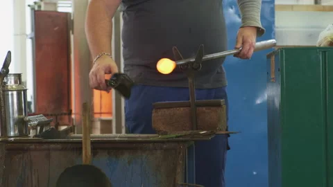 Worker operates with hot glass workpiece on blowpipe in shop Stock Footage 165776944