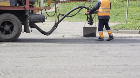 Worker operates specialized road repair machine applying hot asphalt mixture to Stock Footage 344863660