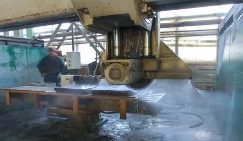 A worker operates a stone cutting machine while water sprays on the material Stock Photos
