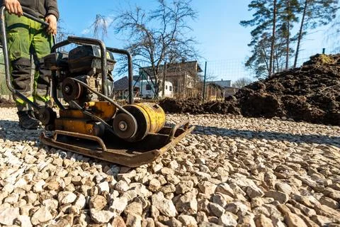 Worker Operates Yellow Plate Compactor on Crushed Stone Driveway Base 写真素材