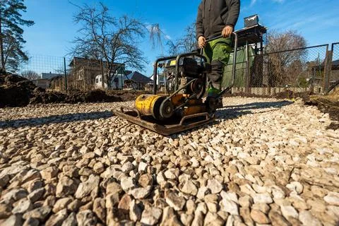 Worker Operates Yellow Plate Compactor on Crushed Stone Driveway Base 写真素材
