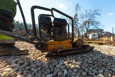 Worker Operates Yellow Plate Compactor on Gravel Driveway Base Stock Photos