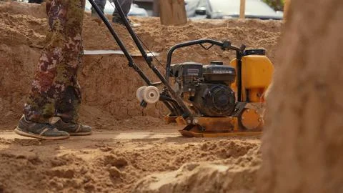Worker operating a compactor compacting soil on construction site Stock Photos