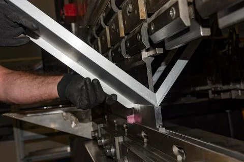 Worker operating metal press machine at workshop. Stock Photos
