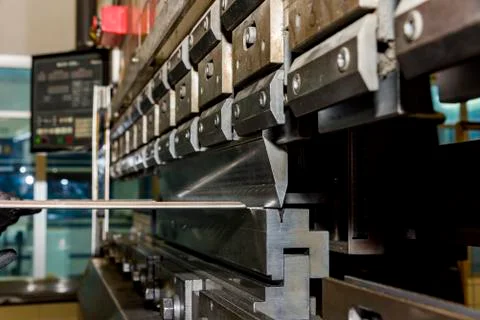 Worker operating metal press machine at workshop. Stock Photos