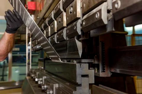 Worker operating metal press machine at workshop. Stock Photos
