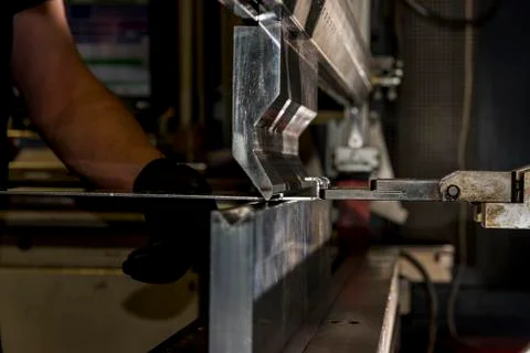Worker operating metal press machine at workshop. Stock Photos