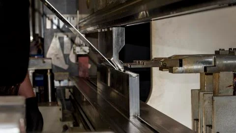 Worker operating metal press machine at workshop. Stock Photos