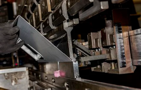 Worker operating metal press machine at workshop. Stock Photos