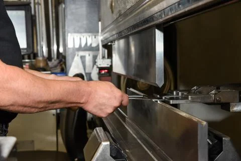 Worker operating metal press machine at workshop. Stock Photos