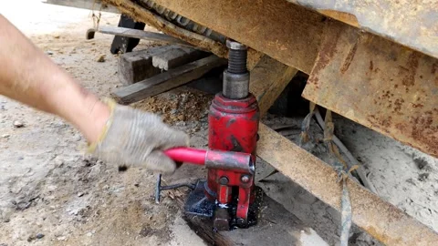 Worker Operating Red Hydraulic Jack in a Construction Setting Stock Footage 305394169