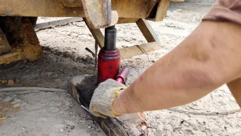 Worker Operating Red Hydraulic Jack in a Construction Setting Stock Footage 305394231