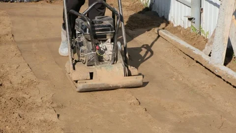 Worker operating a vibrating soil compactor used to compact soil Stock Footage 285865189