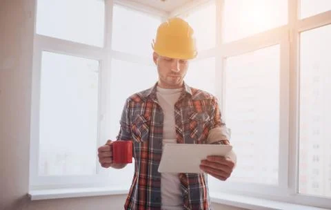 The worker or builder holds a cup of coffee in his hands and looks at the tab Foto stock