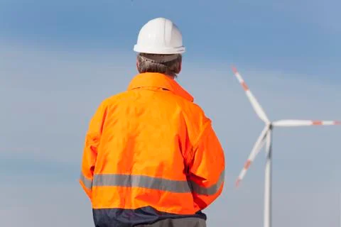 Worker or engineer with hard hat and protective clothing in front of windmill Фото