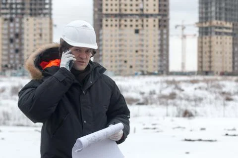 Worker or engineer holding drawing in hands and uses mobile phone on background Stock Photos