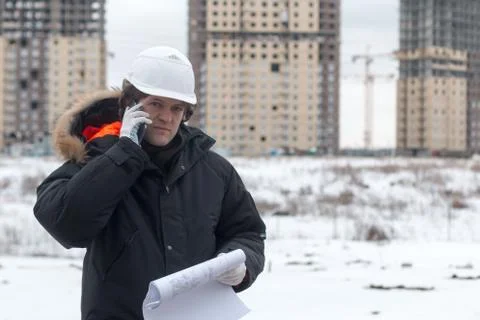 Worker or engineer holding drawing in hands and uses mobile phone on background Stock Photos