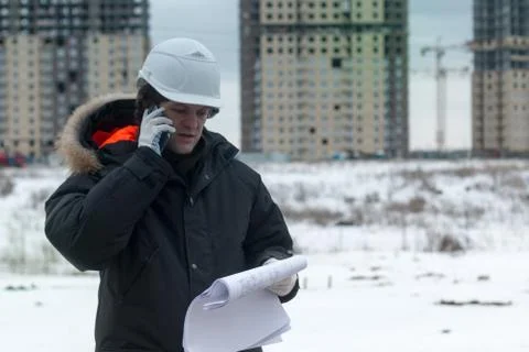 Worker or engineer holding drawing in hands and uses mobile phone on background Stock Photos