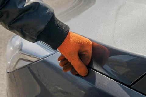 Worker in orange gloves has his hand on the hood of a gray auto Stock Photos