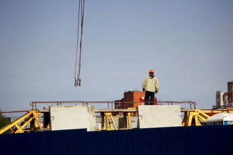 A worker in an orange helmet directs the unloading of concrete slabs with a c Stock Photos