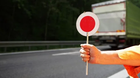 Worker in orange jacket holds out circle sign with red dot as cars drive Stock Footage 252053015