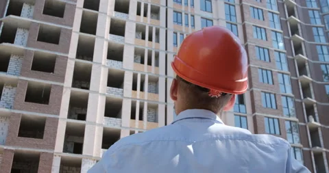 A worker in an orange protective helmet inspects an apartment building Stock Footage 144901434