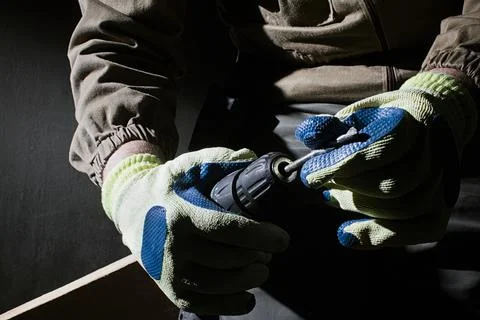 Worker in outfit with blue gloves inserting a drill in socket. Stock Photos