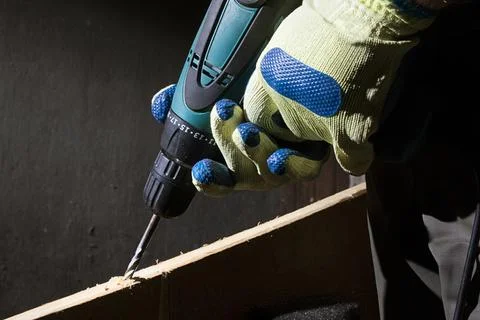 Worker in outfit with blue gloves using drill. Stock Photos