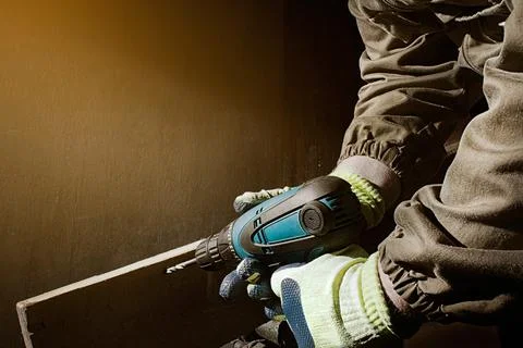 Worker in outfit with blue gloves using drill. Stock Photos
