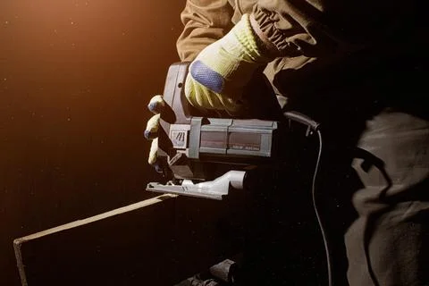 Worker in outfit with blue gloves using electrical jigsaw. Foto stock