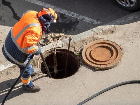 Worker over the open sewer hatch. Repair of sewage, water pipe accident Stock Photos