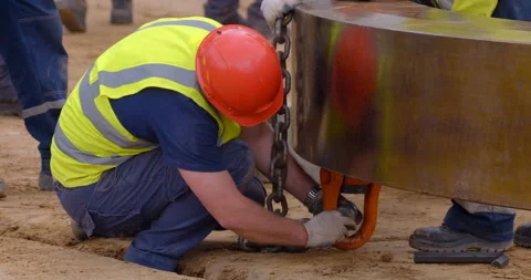 Worker in overalls and a red helmet fixes a metal chain on a large ring Stock Footage 161992981