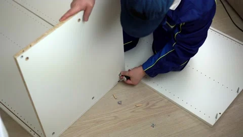 Worker in overalls drives insert screw and tighten with a screwdriver furniture Stock Footage 204842324