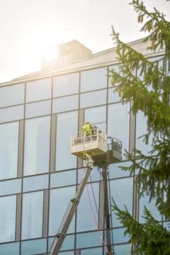 A worker in overalls on an elevator washes the glass wall of a building. Foto stock