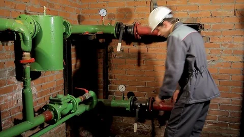 A worker in overalls opens the water valve. The man includes heating in the Stock Footage 77123775
