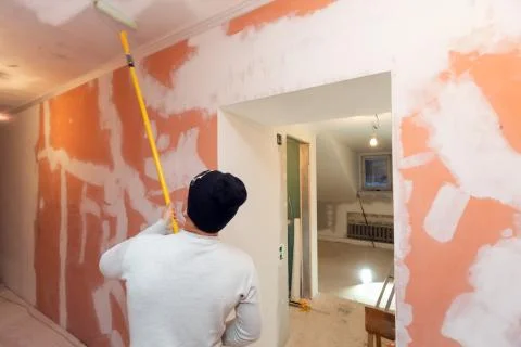 Worker is painting the ceiling by paint roller in corridor an apartment is inder Stock Photos