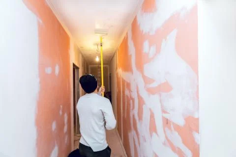 Worker is painting the ceiling by paint roller in corridor an apartment is inder Stock Photos